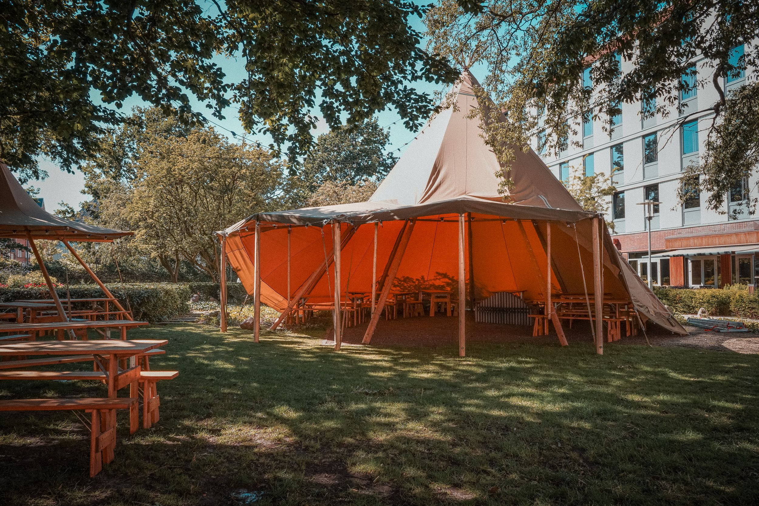 Large outdoor event tent beside picnic tables in a park, showing shade and weather protection for festival visitors.